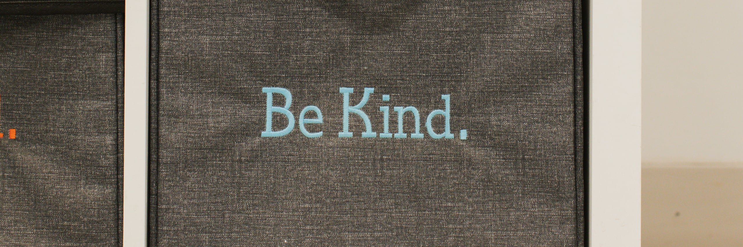 Dark textured fabric panel with the words "Be Kind." printed in light blue lettering