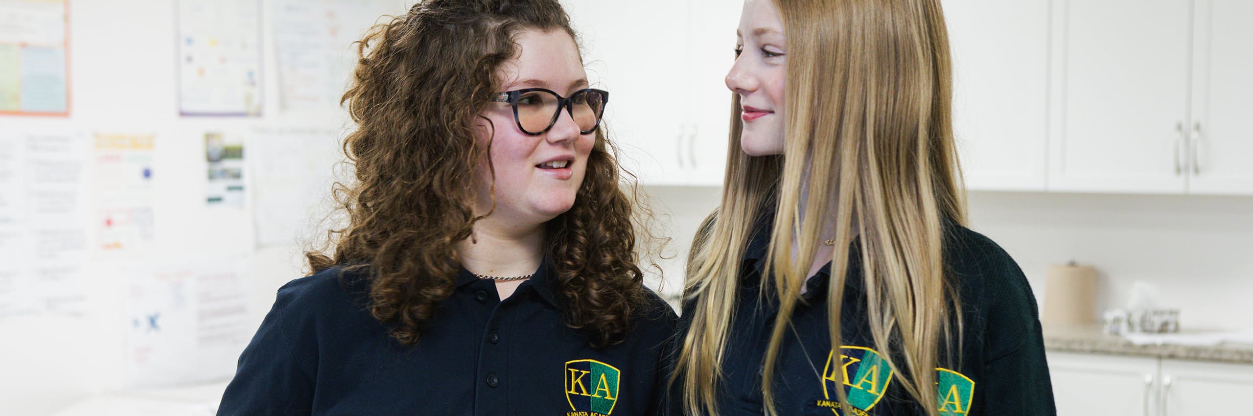 Two Kanata Academy students in school uniform talking, with KA crests visible on their black tops