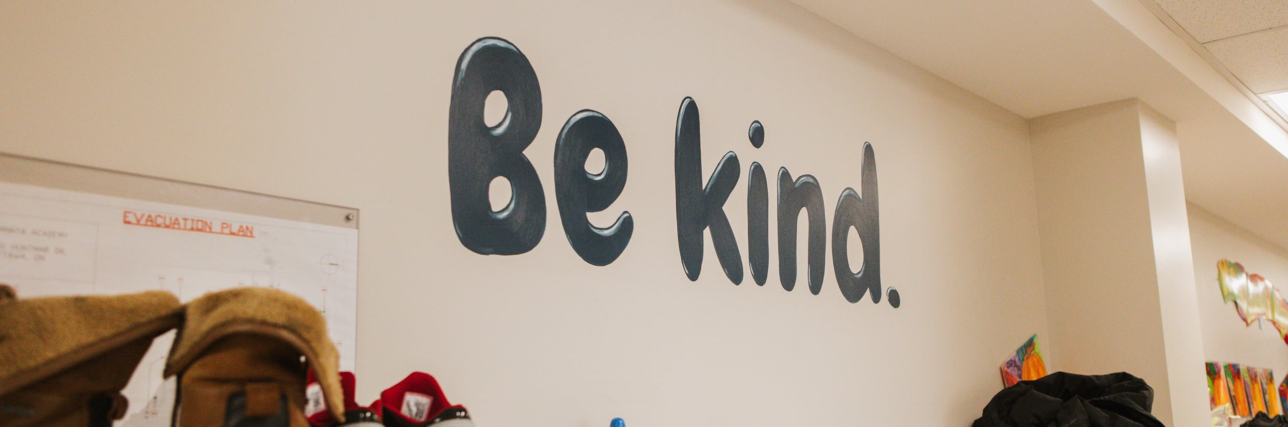 Classroom wall painted with the words "Be kind." with an evacuation plan poster visible to the left