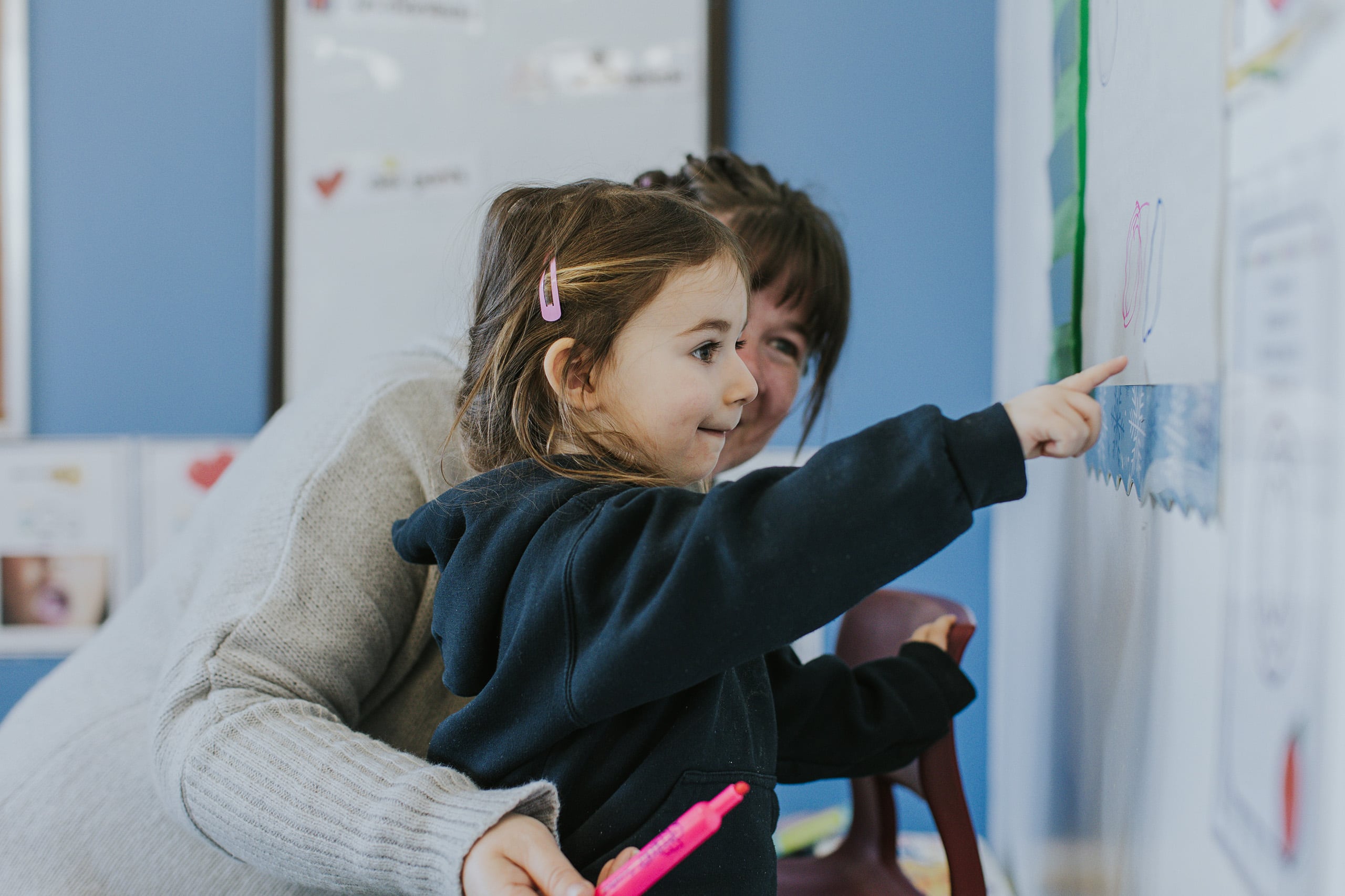 A student pointing at a drawing on a classroom wall.